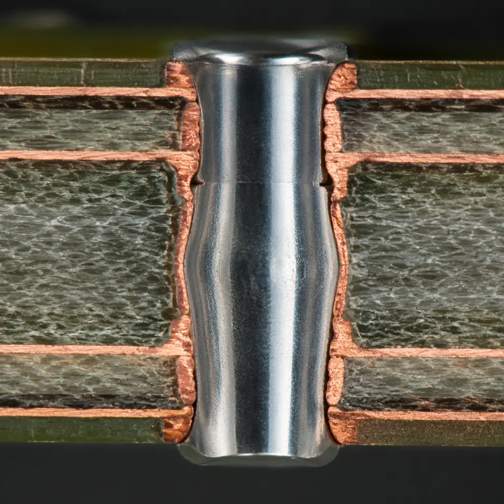 Polished cross-section micrograph of press-fit pin inside PCB plated through-hole, showing compliant pin deformation and copper barrel contact zones under optical microscope